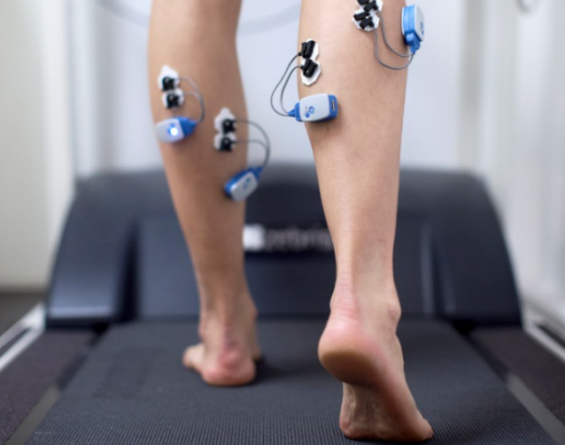 A person with sensors attached to their calves is walking barefoot on a treadmill for a biomechanical study.