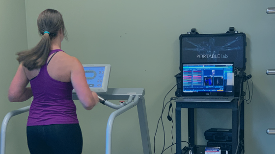 A person in a purple tank top is running on a treadmill next to a setup with a laptop and scientific equipment labeled "Portable lab.