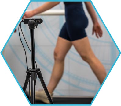 A person walking on a treadmill with a camera mounted on a tripod in the foreground.