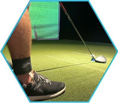 Person's leg and golf club on an indoor golfing green, ready to hit a ball.