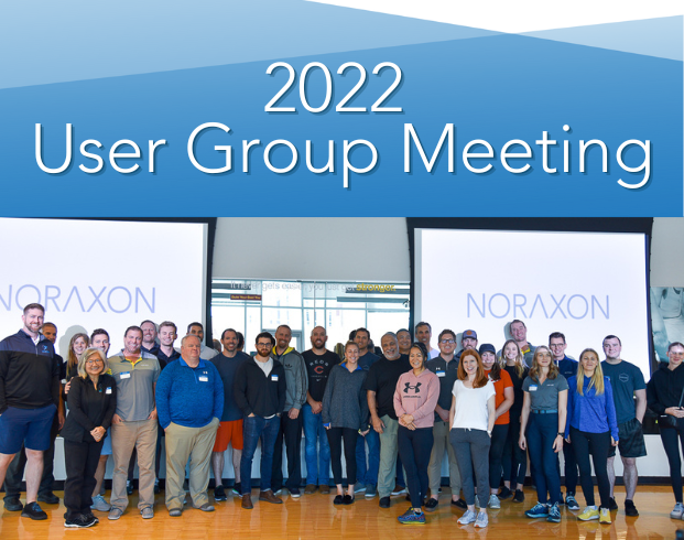 Group of people smiling and standing together in front of two screens displaying the text 'Noraxon' at the 2022 User Group Meeting.