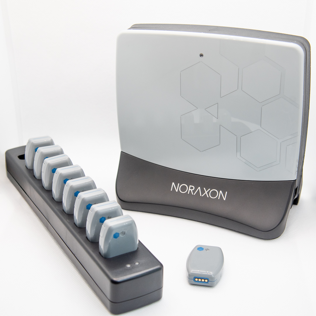 A Noraxon wireless sensor system includes a docking station with multiple sensors and a larger base unit designed for biomechanical and physiological data collection.