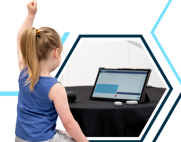 A child raises their arm while sitting at a table with a tablet and two small devices.